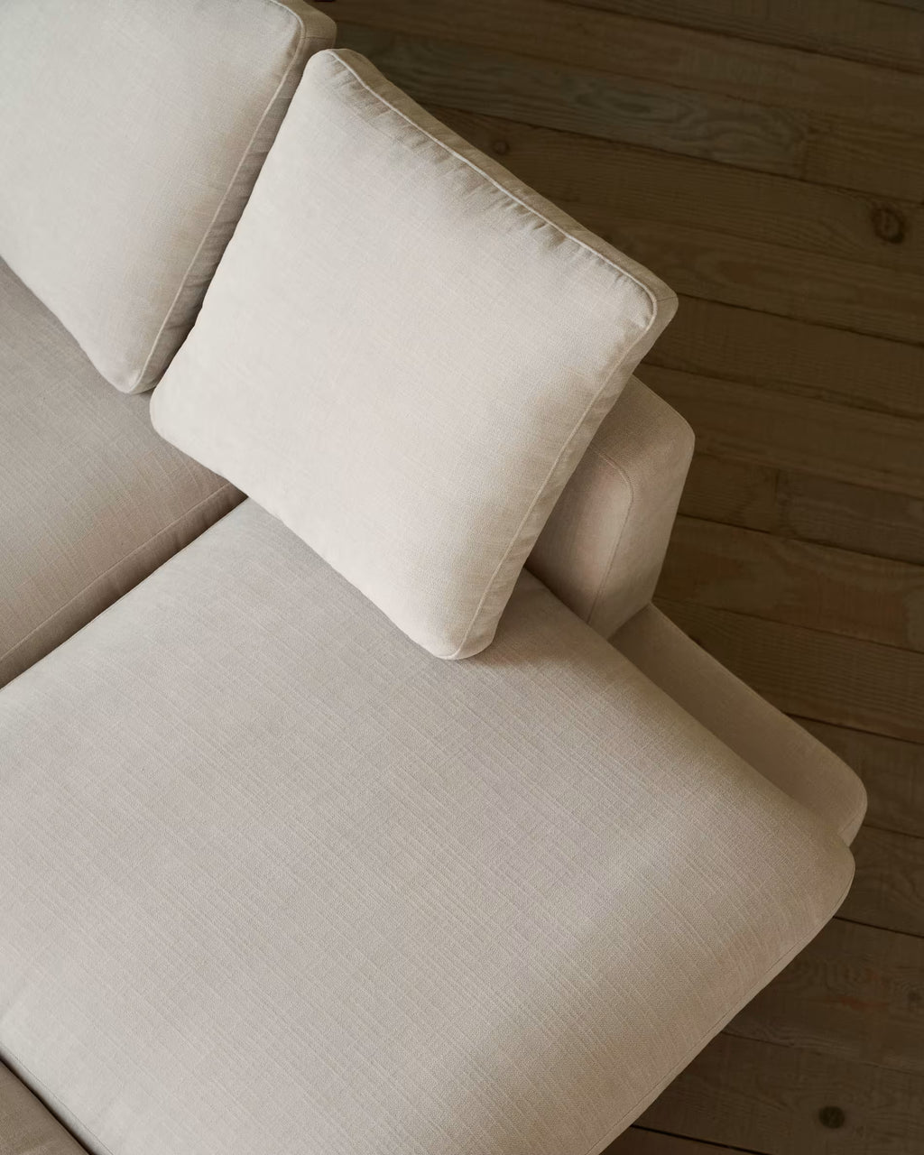 Beige sectional sofa with a pillow on a wooden floor.