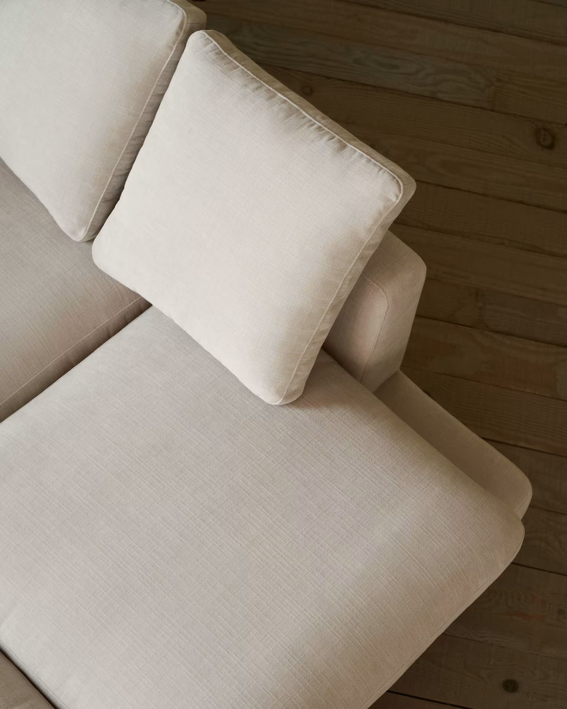 Beige sectional sofa with a pillow on a wooden floor.