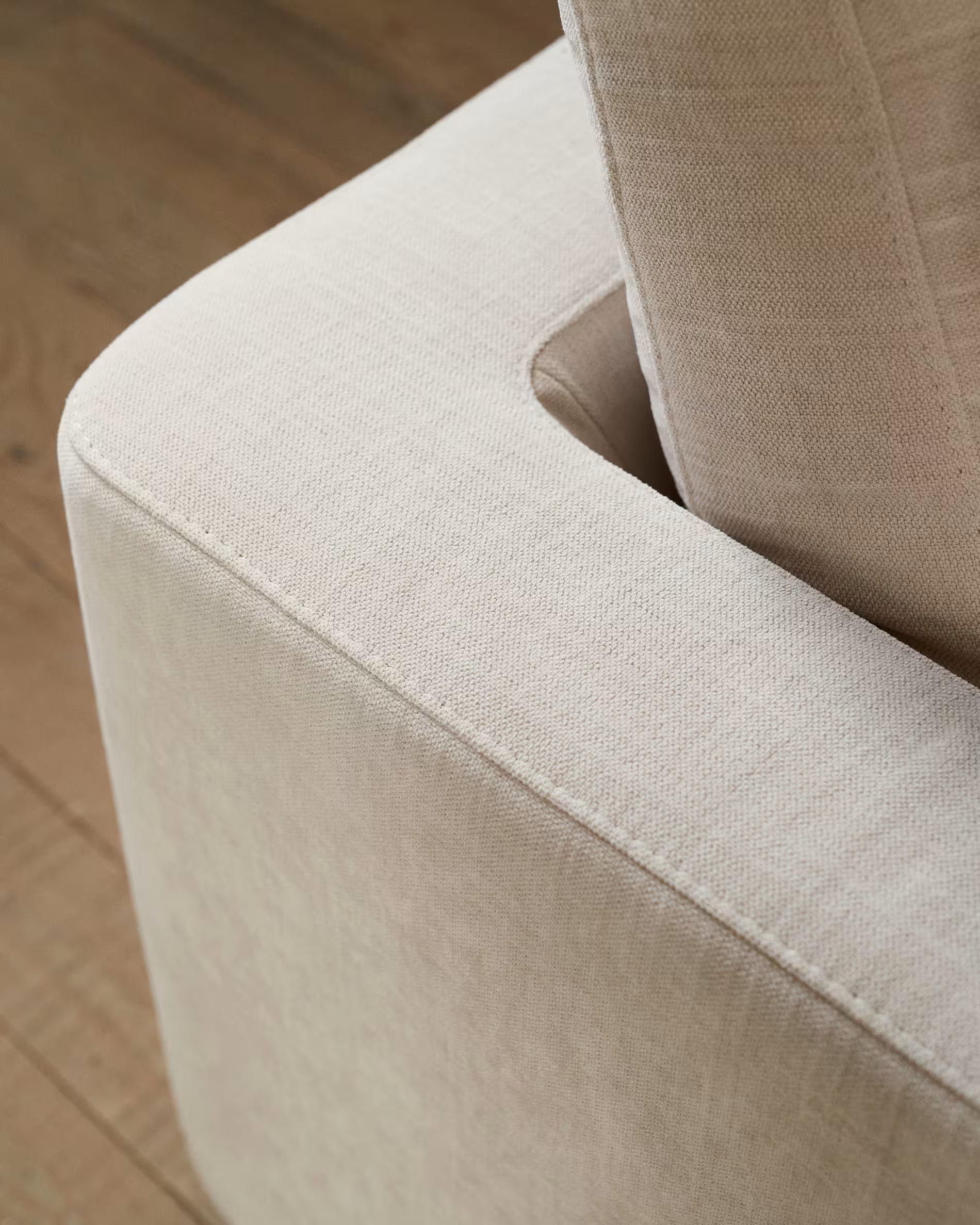 Close-up of a beige upholstered chair corner on a wooden floor.