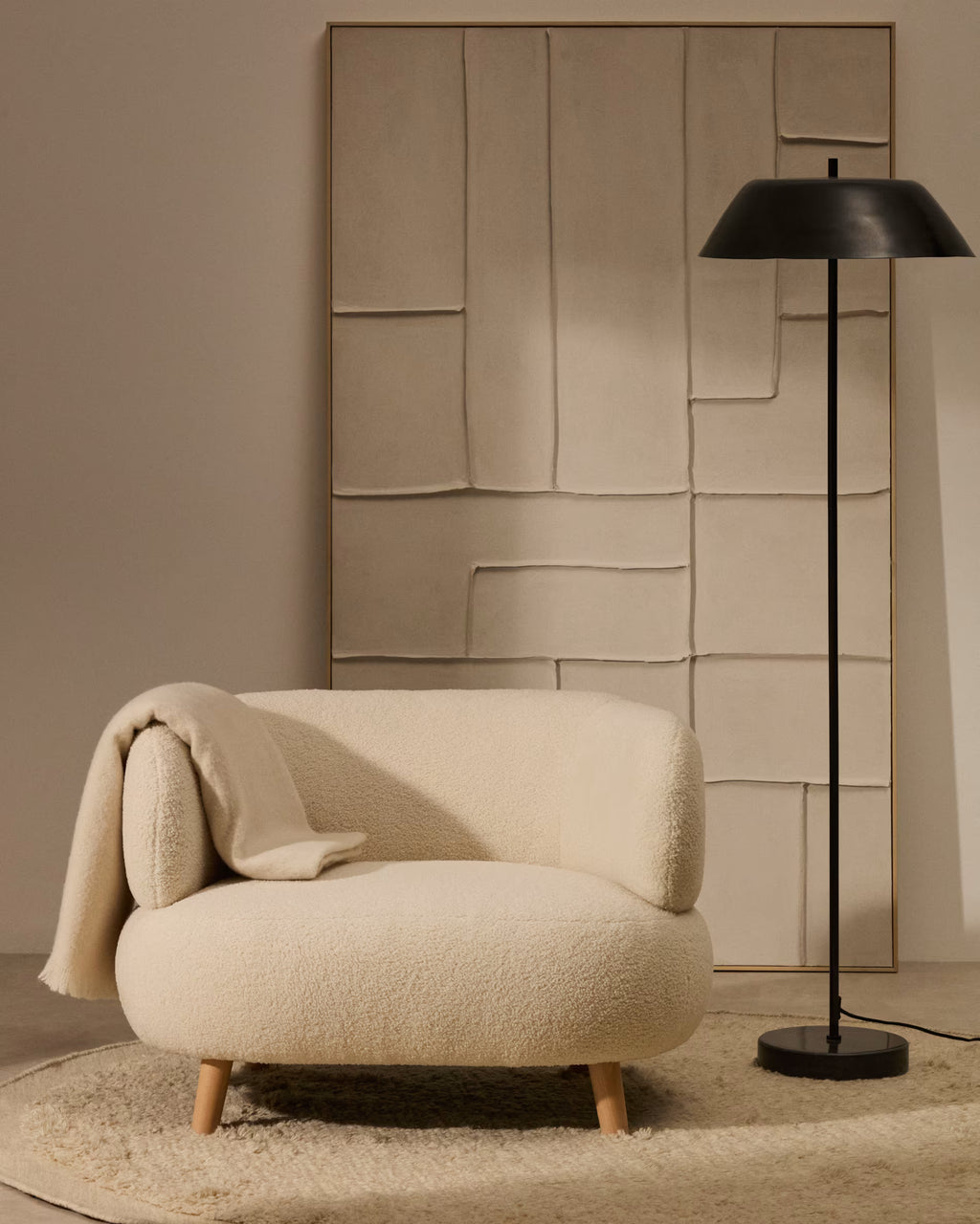 Beige armchair with a blanket and black floor lamp against a textured wall.
