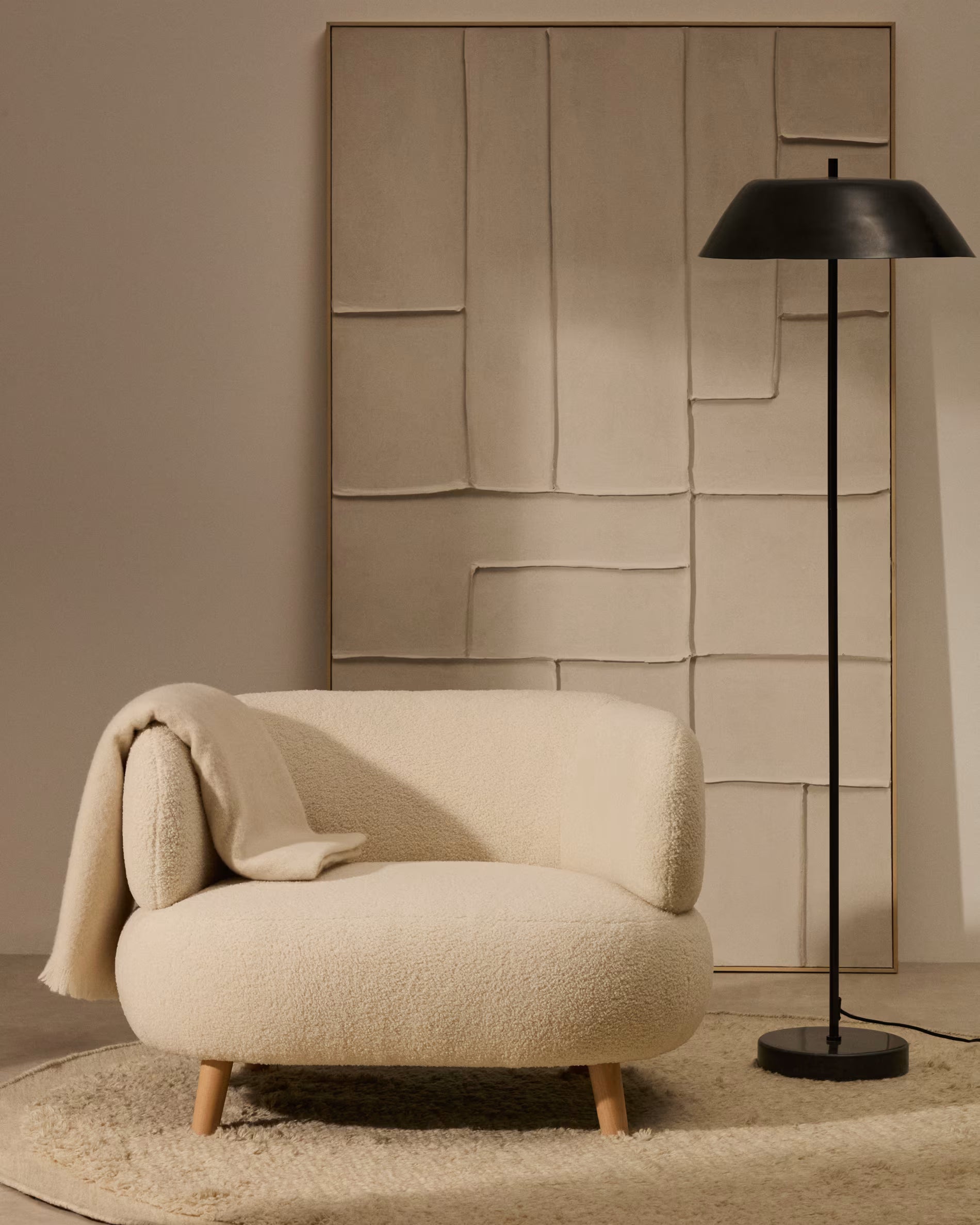 Beige armchair with a blanket and black floor lamp against a textured wall.