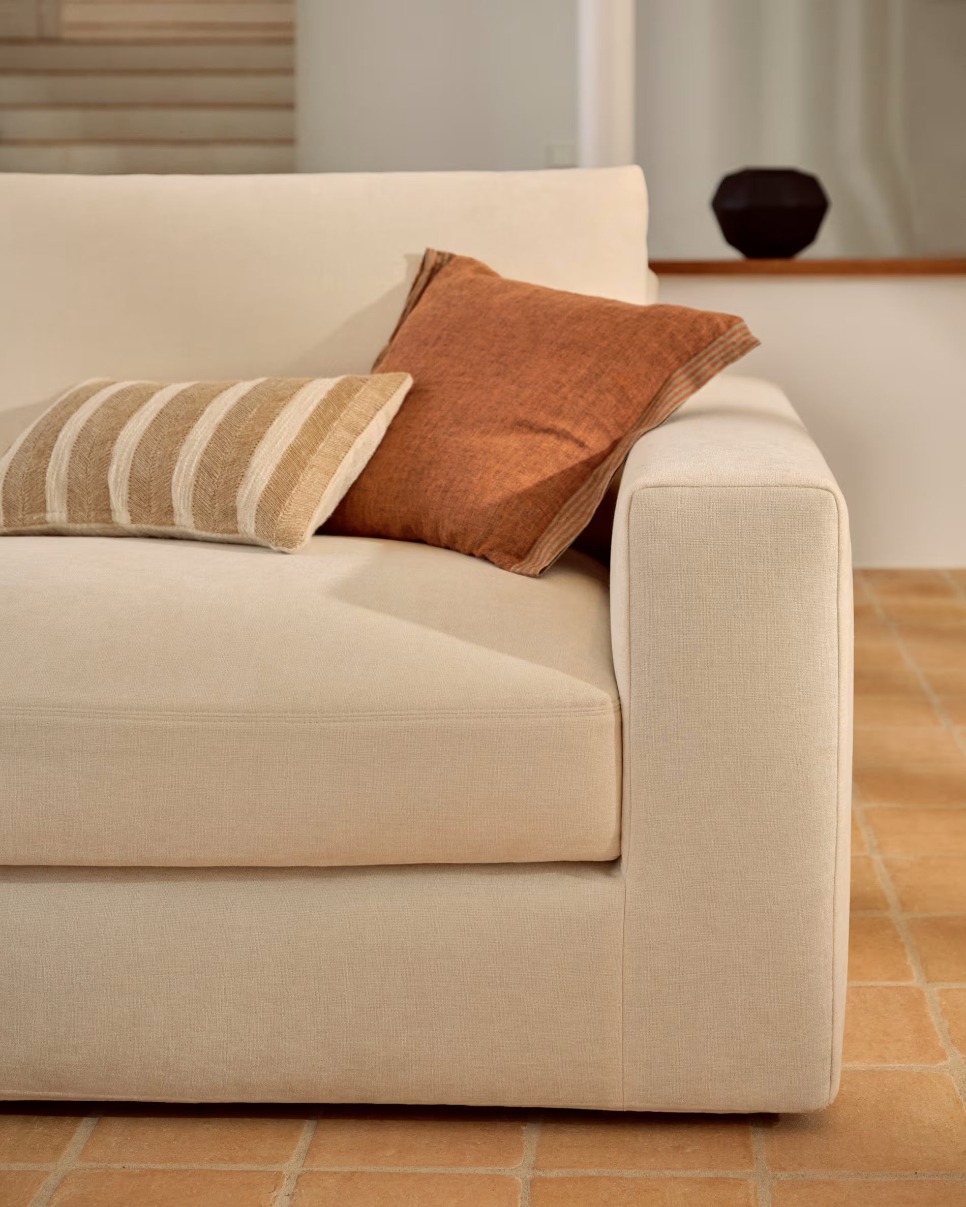 Beige sofa with two pillows on a tiled floor