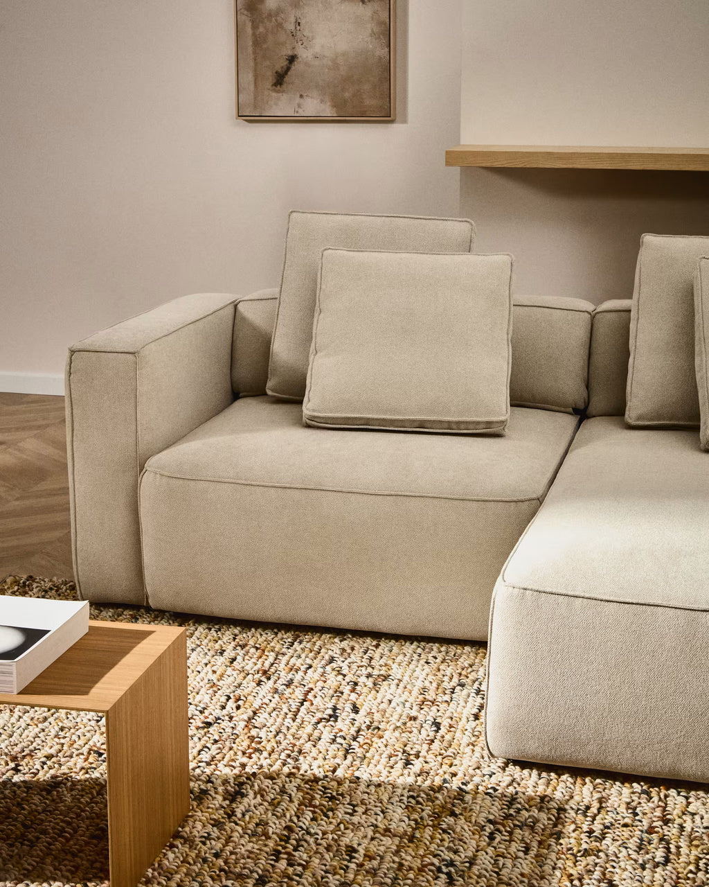 Beige sectional sofa in a living room setting with a wooden coffee table and abstract art on the wall.